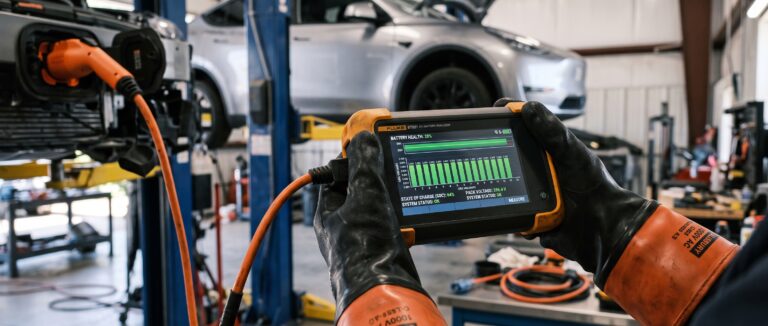 Kfz-Sachverständiger mit Hochvolt-Schutzhandschuhen wertet Messdaten auf einem Diagnosegerät aus – professionelle Batteriediagnose für Kfz-Gutachter an einem E-Auto auf der Hebebühne.